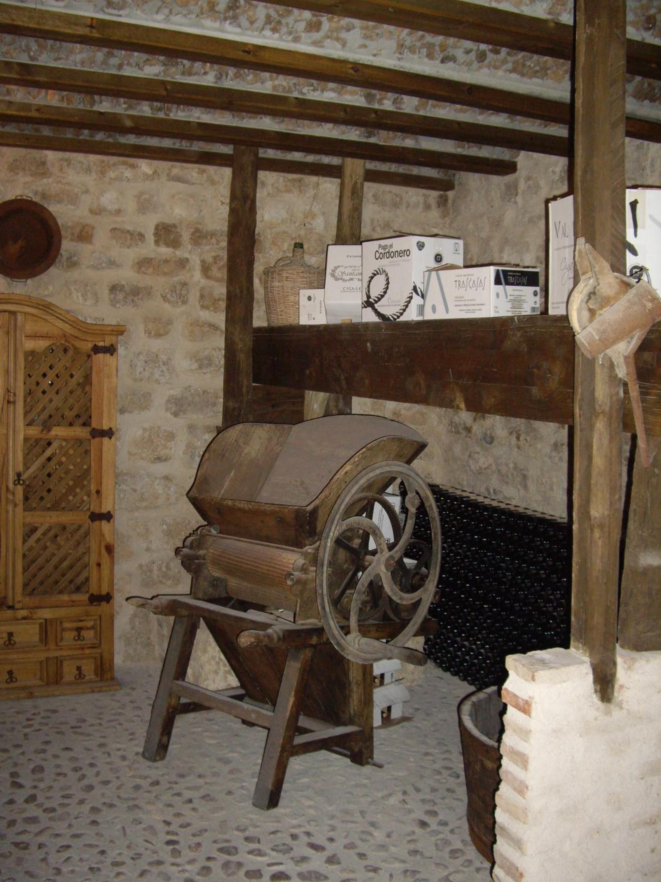 Una habitación rústica con pared de piedra, vigas de madera, un viejo molino de grano y un aparador de madera.