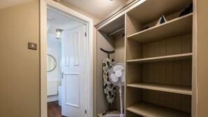Un couloir avec une porte blanche, un radiateur, un miroir, un ventilateur et une étagère.