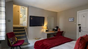 A hotel room with a bed, a desk, a chair, a television, and a staircase leading to a bathroom.