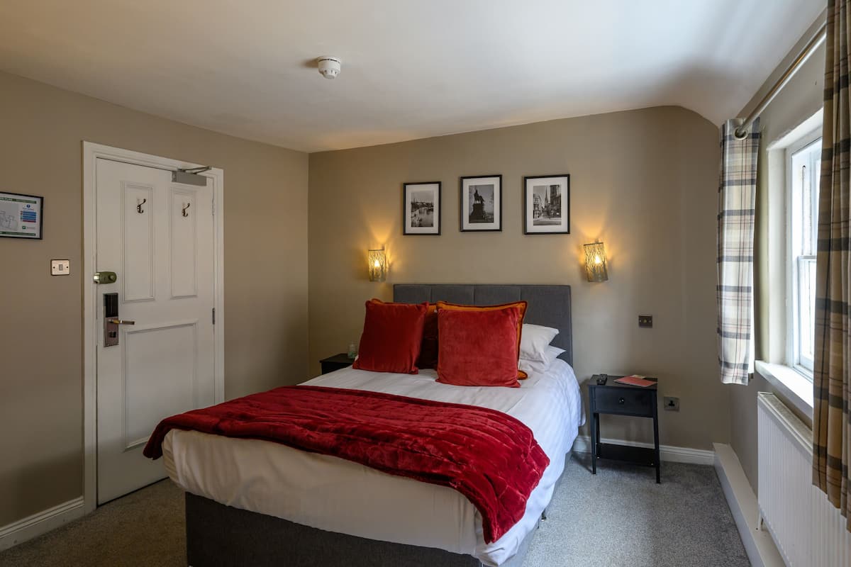 A bedroom with a bed, two bedside tables, a door, and three framed pictures on the wall.