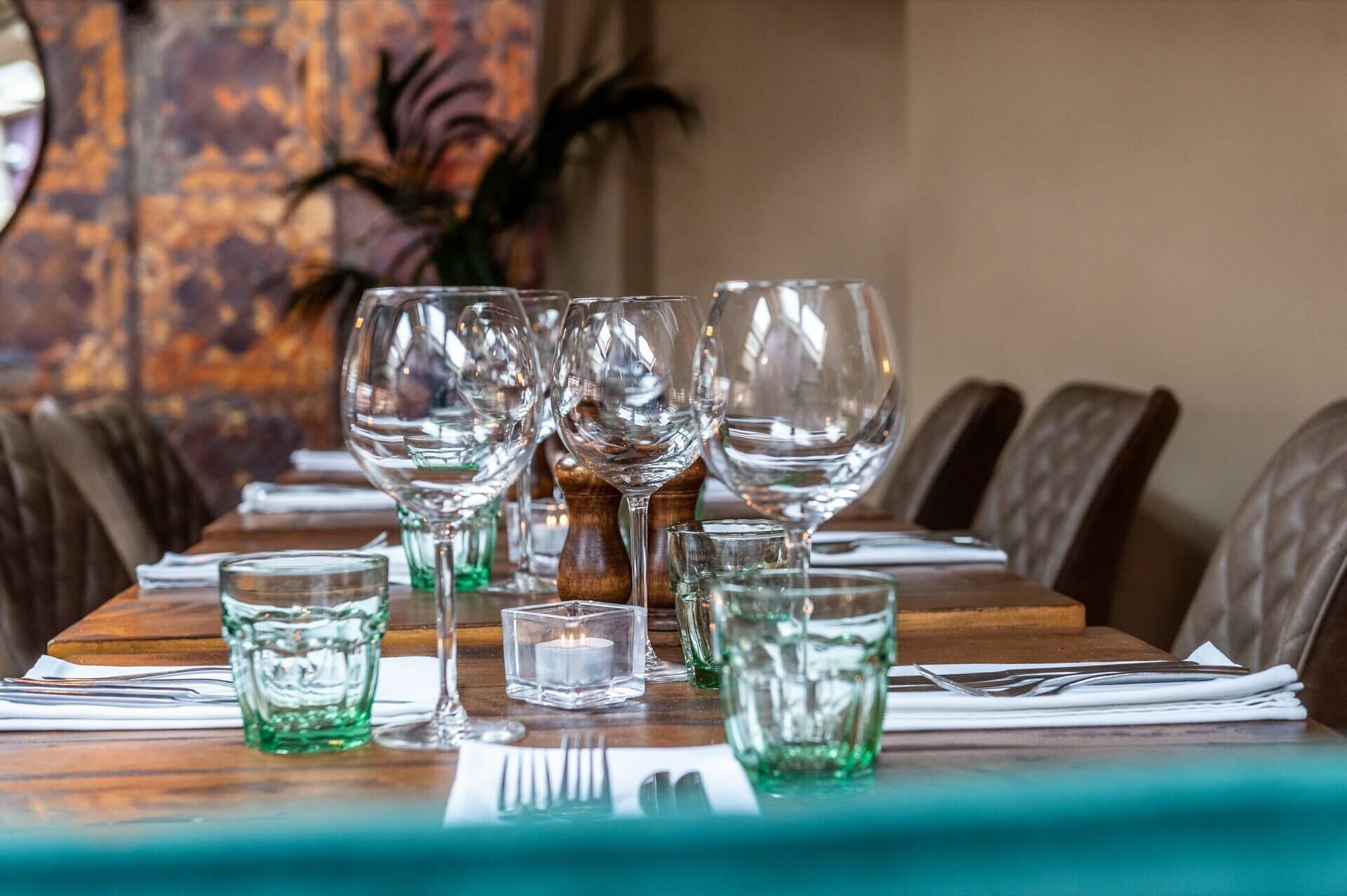 A dining table set with multiple wine glasses, small glasses, and a candle.