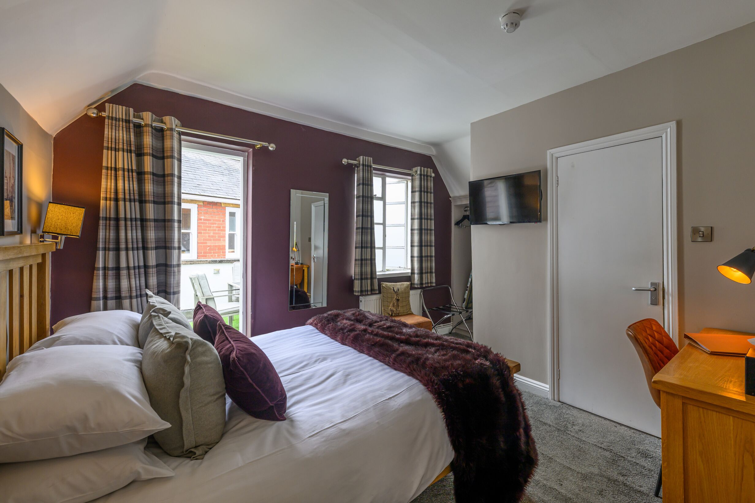 A bedroom with a bed, a desk, a chair, a television, and a window with curtains.