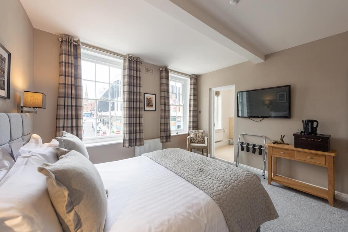 A hotel room with a large bed, a desk, a chair, a television, and a window with curtains.