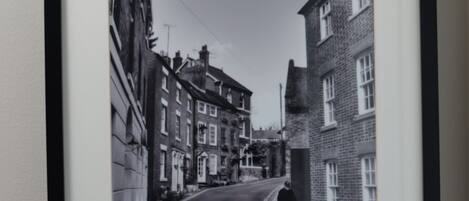 A framed black and white photograph of a street with buildings and a cyclist, captioned 'The Loopy Shrew 2011 Belmont.'