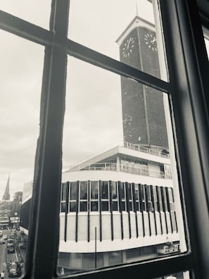 A view through a window of a building with a clock tower, a modern building with vertical lines, and a busy street with cars. - The Loopy Shrew (Shrewsbury)