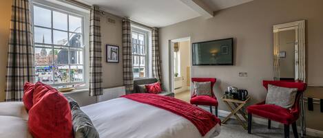 Ett hotellrum med en stor säng, två röda fåtöljer, ett litet bord med en vattenkokare, en tv och utsikt över staden.
