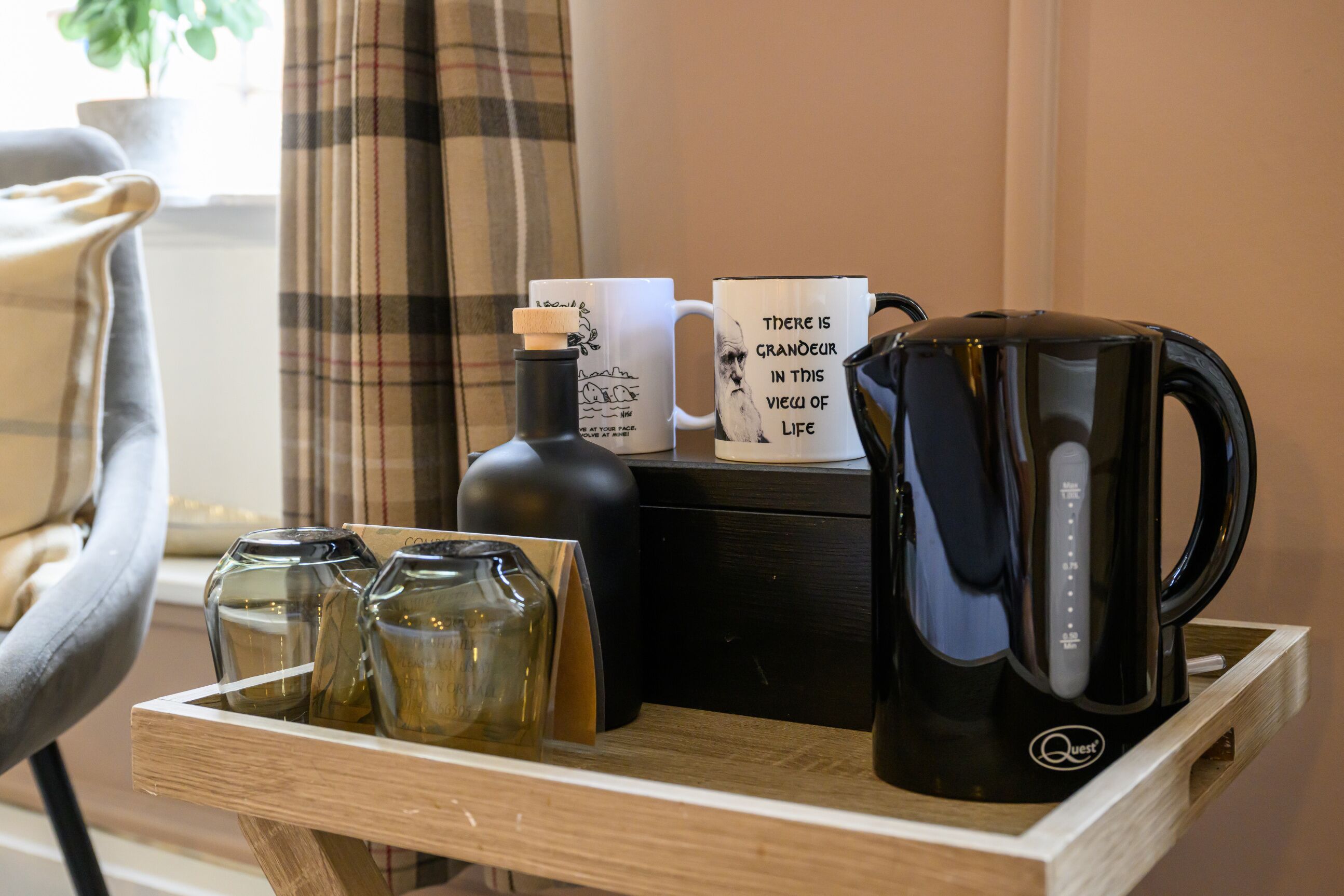 A tray with a black coffee maker, two mugs, and three glass bottles.