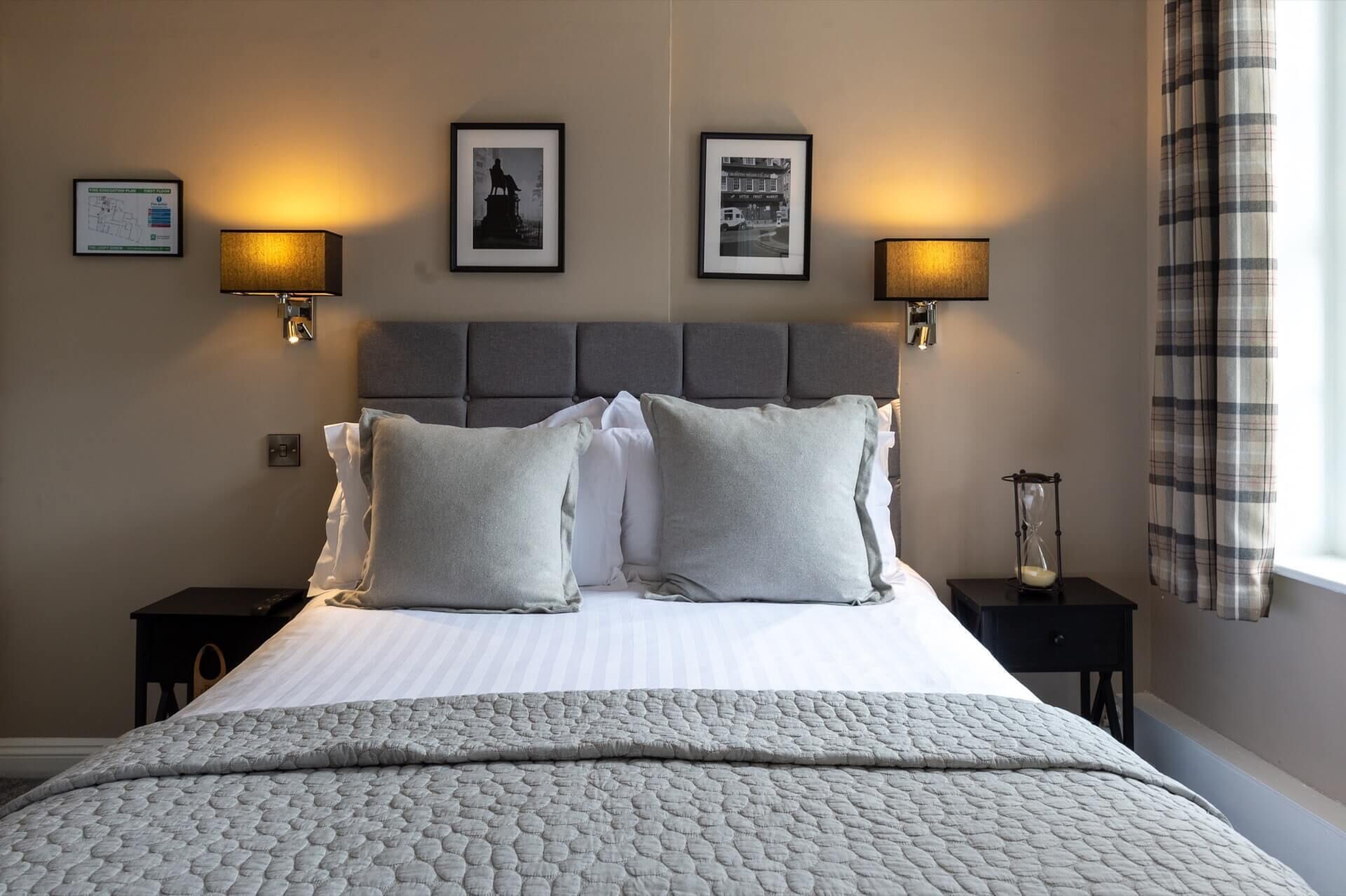 A neatly made bed with a grey quilt, two bedside tables with lamps, and framed pictures on the wall.