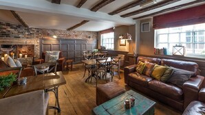 A rustic interior with exposed wooden beams, a brick wall, a fireplace, a dining area, and a leather sofa. - The Loopy Shrew (Shrewsbury)