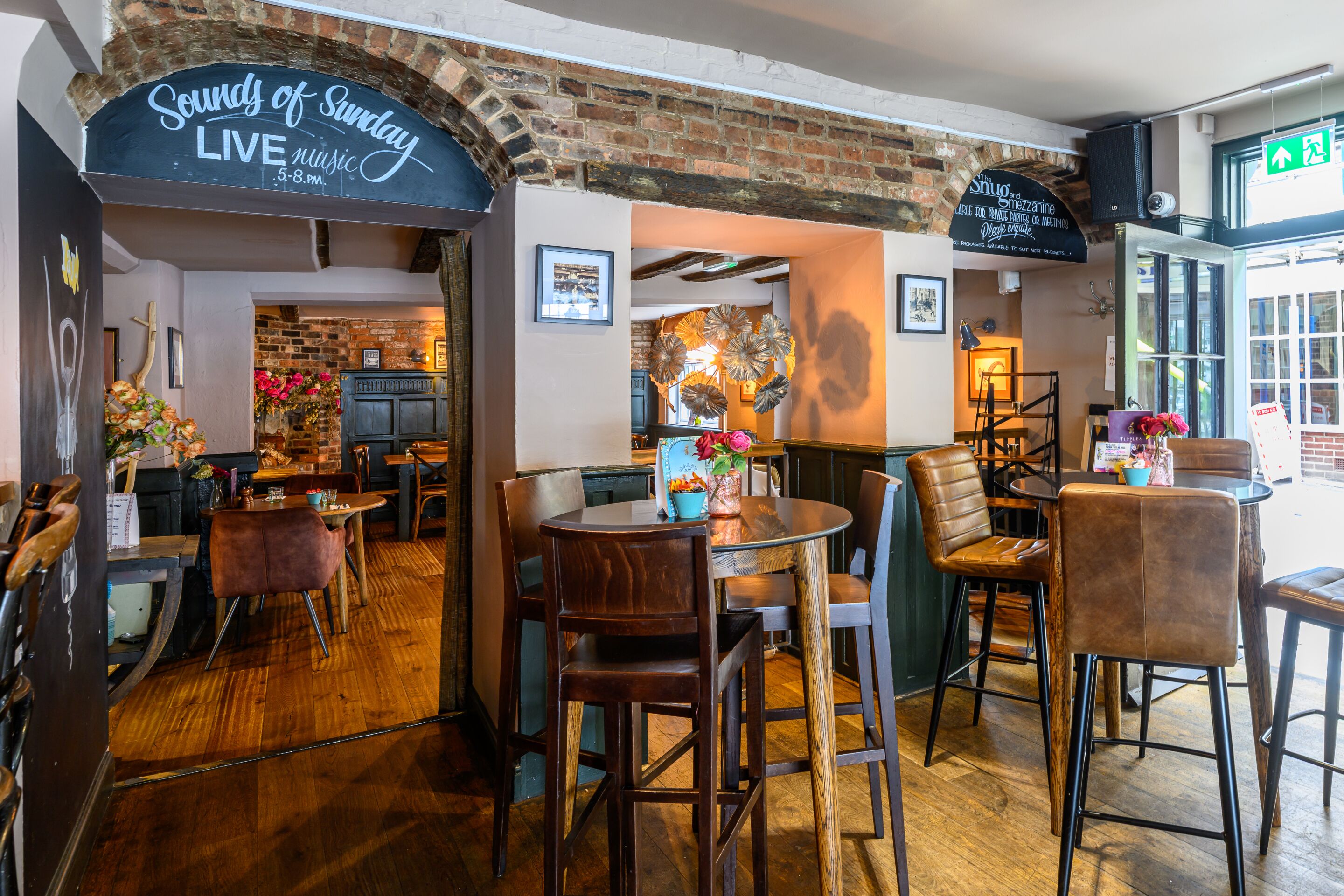 A restaurant interior with brick walls, wooden flooring, and a variety of seating arrangements including tables and chairs.