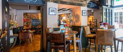 A restaurant interior with brick walls, wooden flooring, and a variety of seating arrangements including tables and chairs.