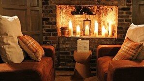 Un coin salon accueillant avec des fauteuils en cuir, un mur en pierre et des bougies créant une ambiance chaleureuse.