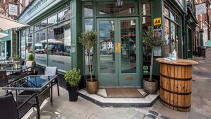 A corner building with a green facade, a glass storefront, outdoor seating, and a wooden barrel. - The Loopy Shrew (Shrewsbury)