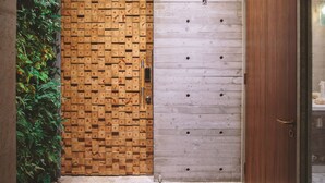 Ein Korridor mit einer Holztür, einer Betonwand und einer Glastür zu einem Raum.