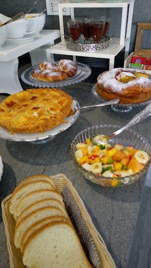 A buffet with various food items including a fruit salad, pastries, and bread. - Cascina Beatrice (Rodello)