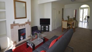 A living room with a fireplace, a sofa, a television, and a dining area with a table and chairs. - Victorian Rose Cottage (Deal)