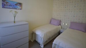 A bedroom with two single beds, a dresser, and a painting on the wall. - Victorian Rose Cottage (Deal)