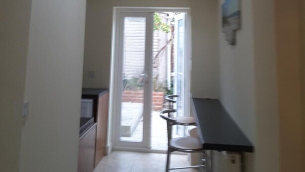 A narrow hallway with a skylight, a door leading to a patio, and a bar area with stools. - Victorian Rose Cottage (Deal)
