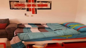 A bedroom with a bed, a small table, and a wall-mounted artwork. - Les Residences Rima 9 (Abidjan)