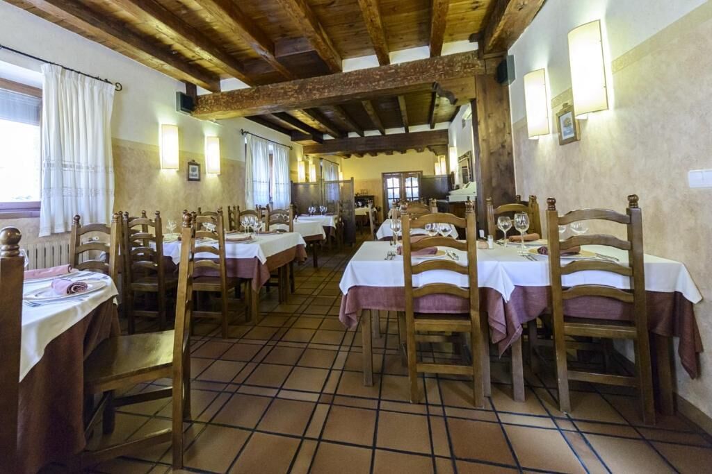 A restaurant with wooden tables and chairs, white tablecloths, and tiled flooring.