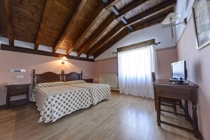 Un dormitorio con techo de madera, una cama con colcha estampada, un escritorio con computadora y una ventana con cortinas.