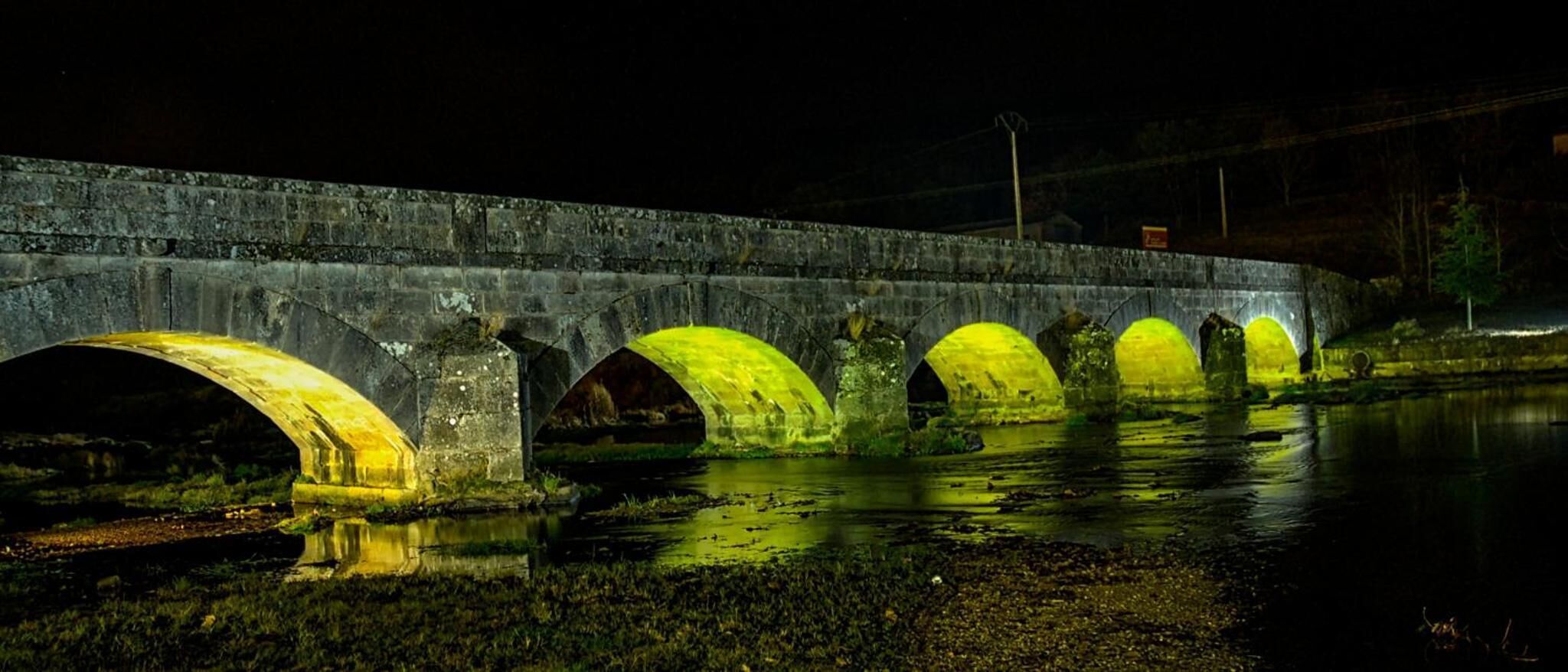 A bridge with multiple arches illuminated by yellow lights at night.