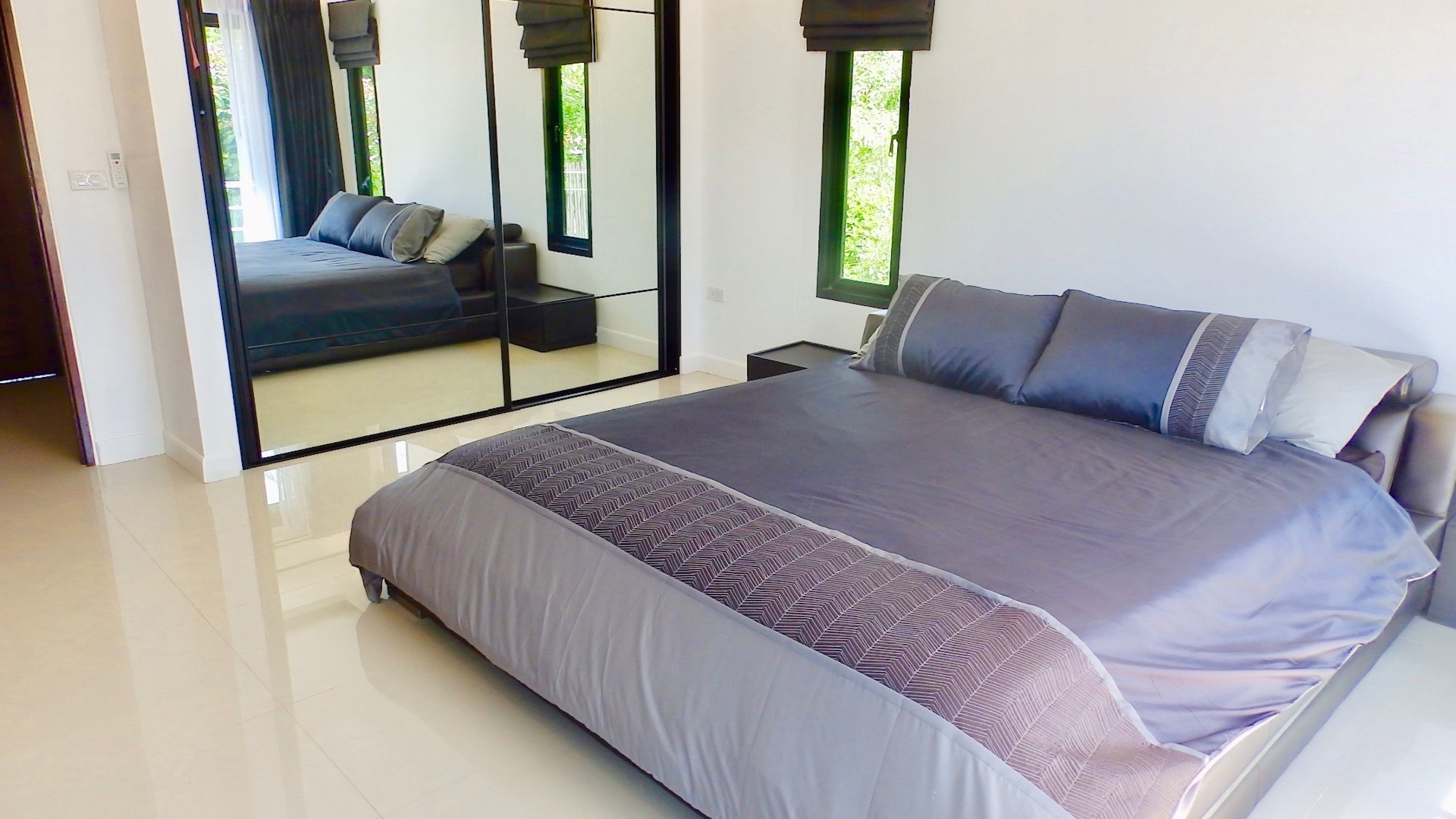 A modern bedroom with a large bed, a mirror, and a view of greenery outside.