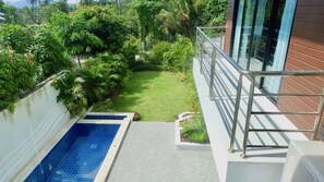 Uma piscina no terraço com guarda-corpo de vidro, rodeada por vegetação exuberante e uma vista desimpedida da paisagem urbana.