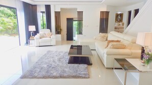 A modern living room with a white sofa, a coffee table, and a rug. There is a chair and a lamp in the corner. - 3 Bedroom Private Pool Villa Flora (Koh Samui)