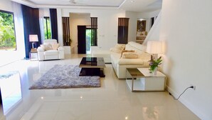A modern living room with a sofa, coffee table, and a rug. There is a staircase leading to another level. - 3 Bedroom Private Pool Villa Flora (Koh Samui)