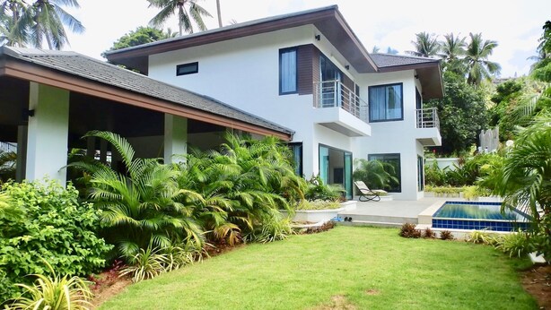 A modern two-story house with a covered patio, a swimming pool, and lush tropical vegetation. - 3 Bedroom Private Pool Villa Flora (Koh Samui)
