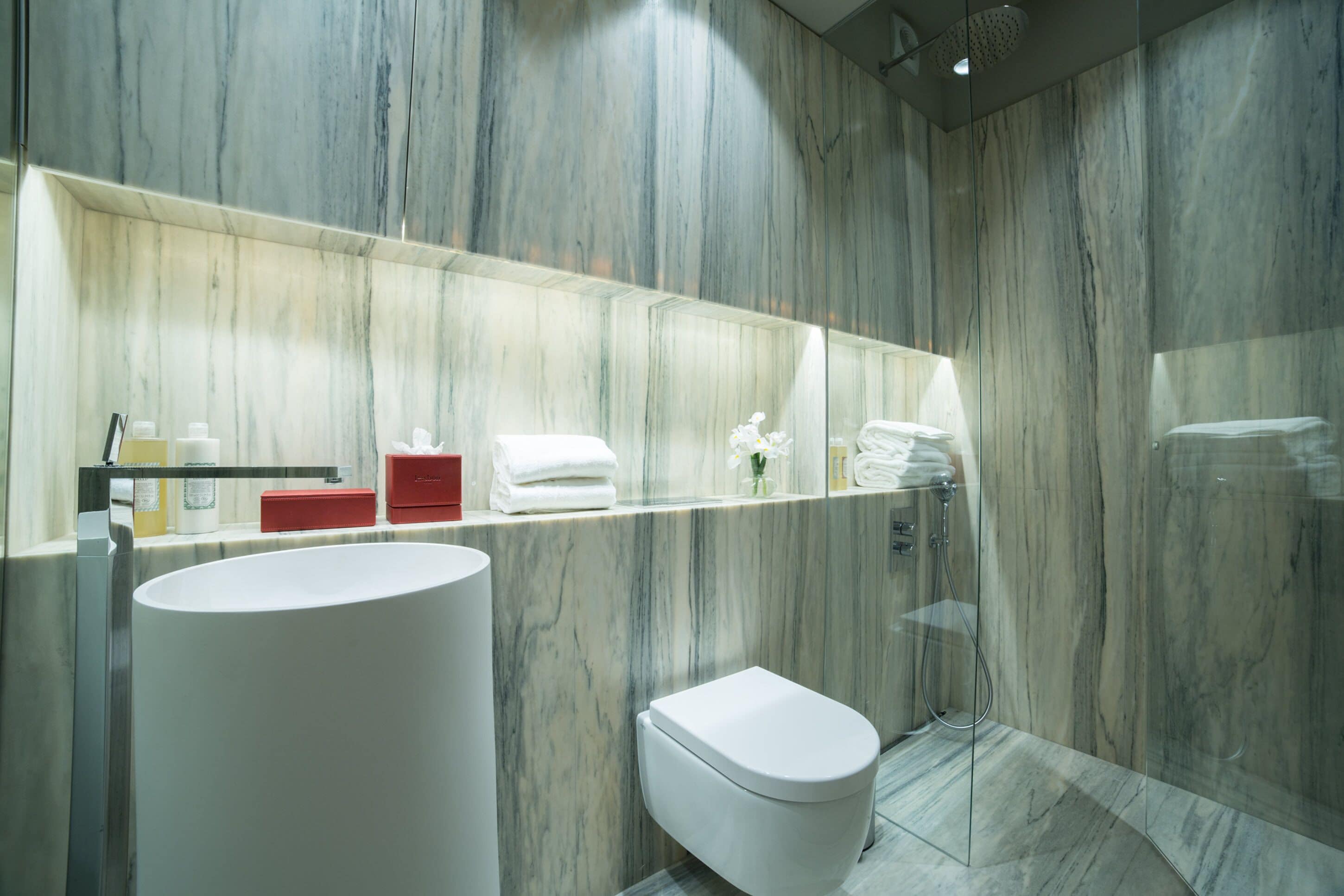 Een moderne badkamer met een marmeren wand, een groot wastafel, een toilet en een douchecabine.