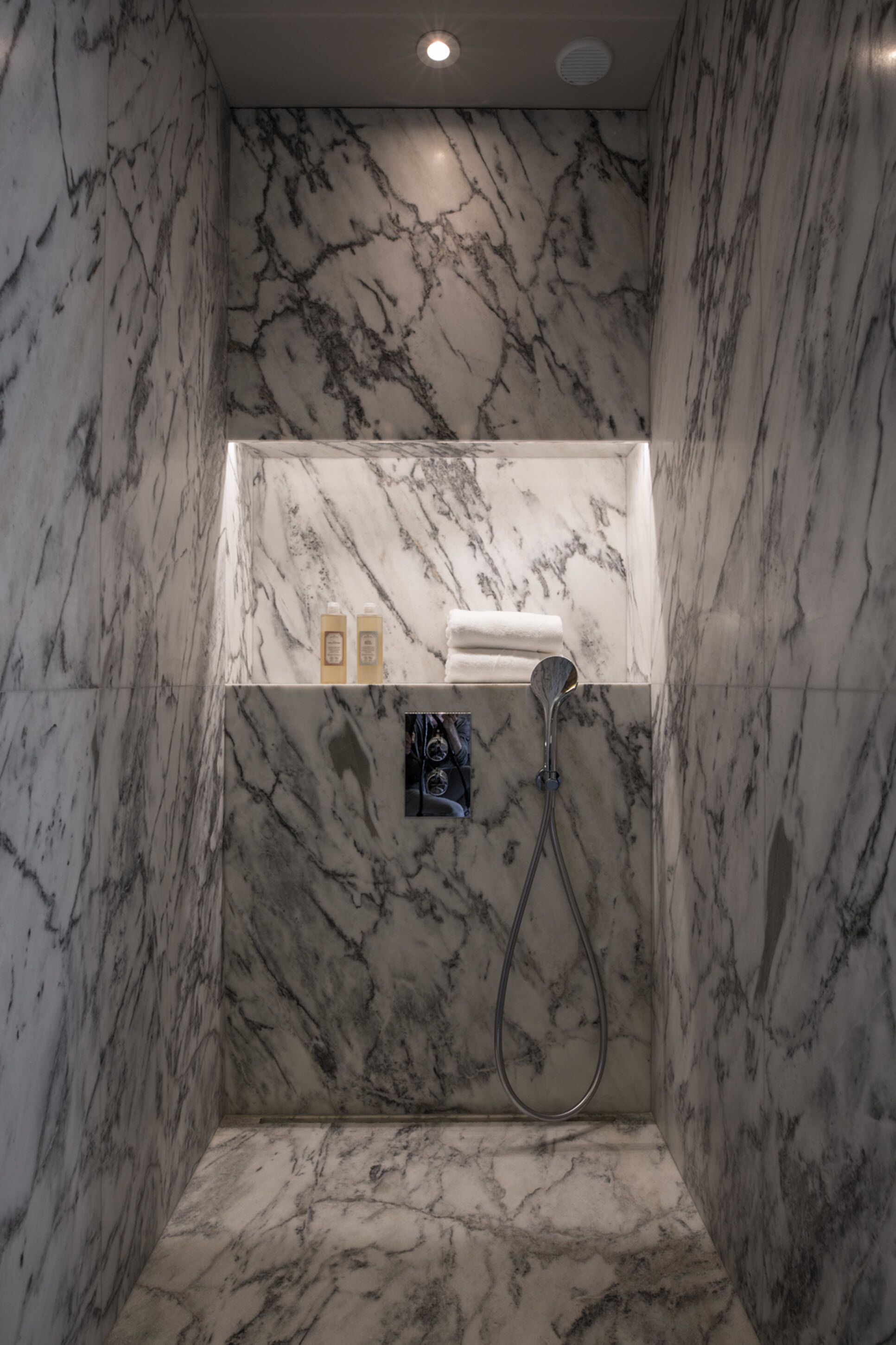 Une salle de bain en marbre avec une douche, une étagère pour les articles de toilette et un porte-serviettes.