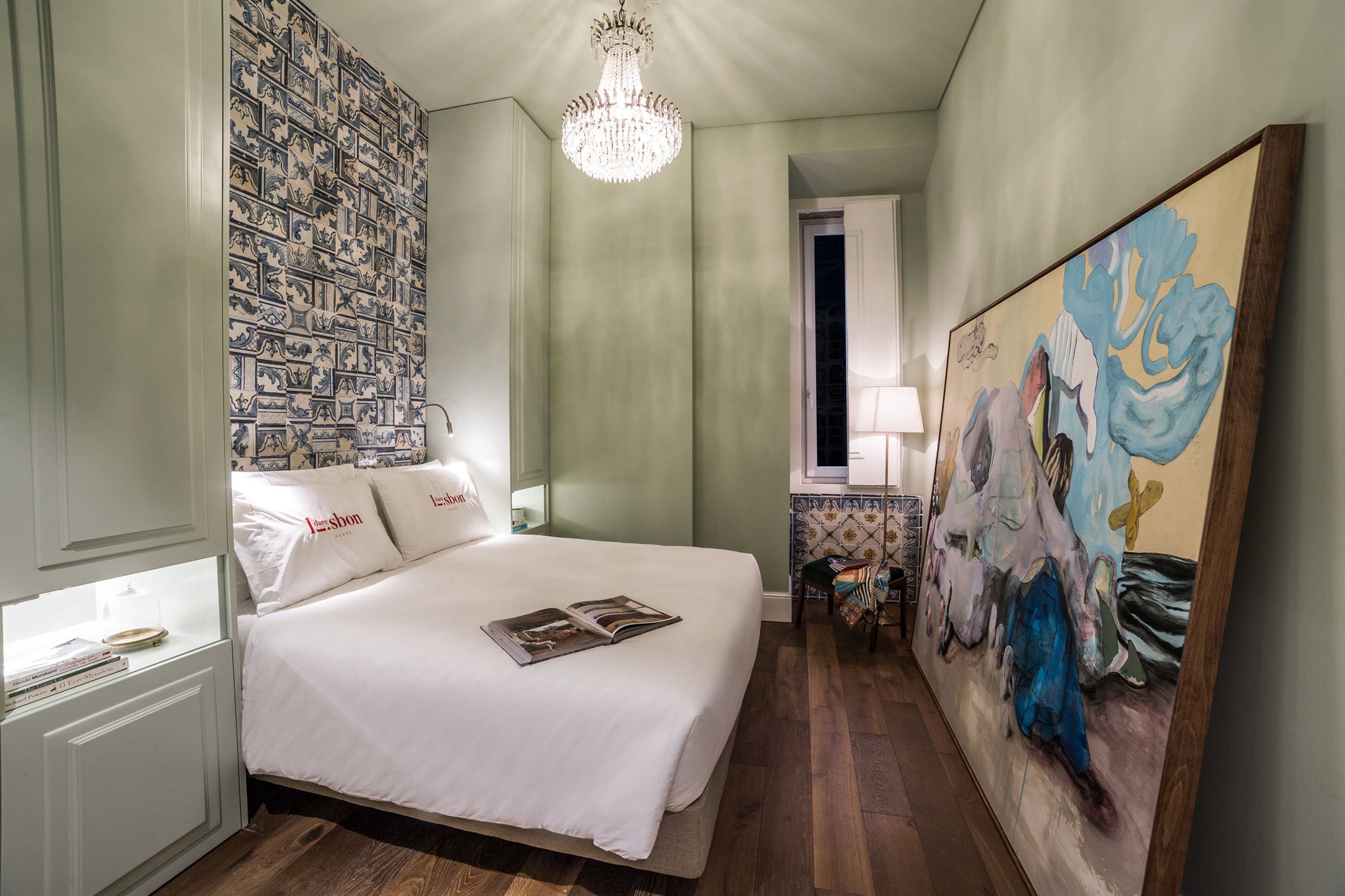 A hotel room with a large bed, a chandelier, a painting, and a patterned wall.