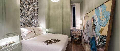 A hotel room with a large bed, a chandelier, a painting, and a patterned wall.