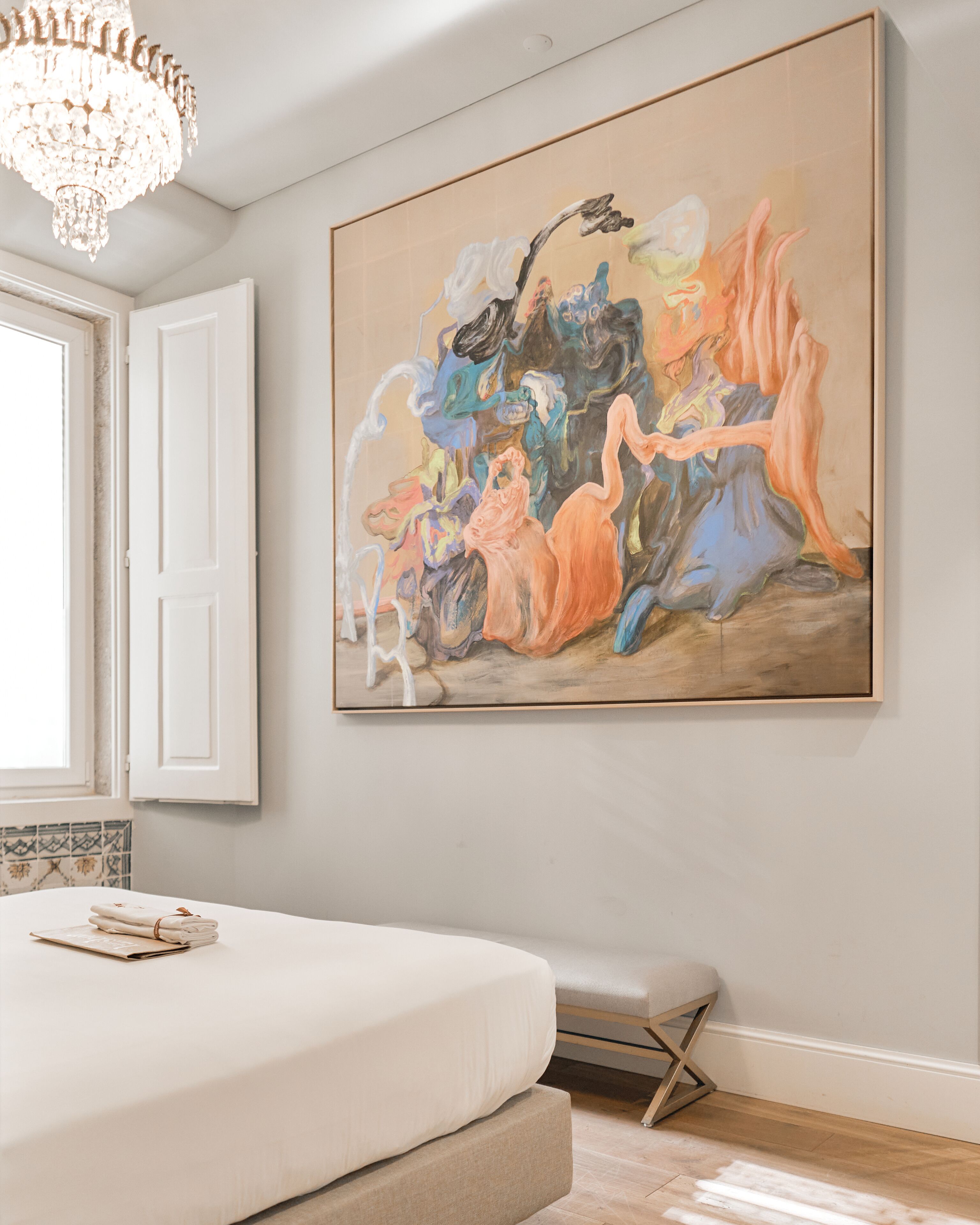 A bedroom with a large abstract painting on the wall, a bed, a bench, and a chandelier.