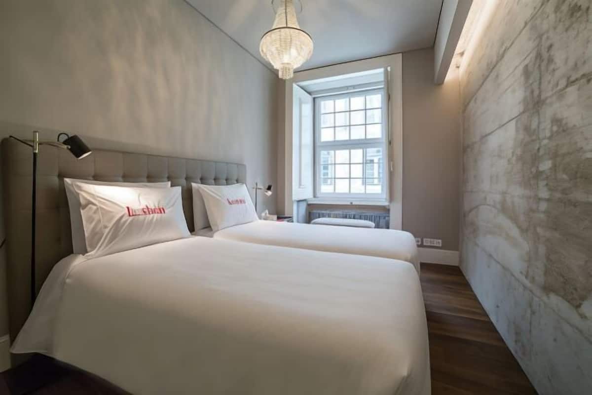 Une chambre avec deux lits, une grande fenêtre, un lustre et un radiateur.