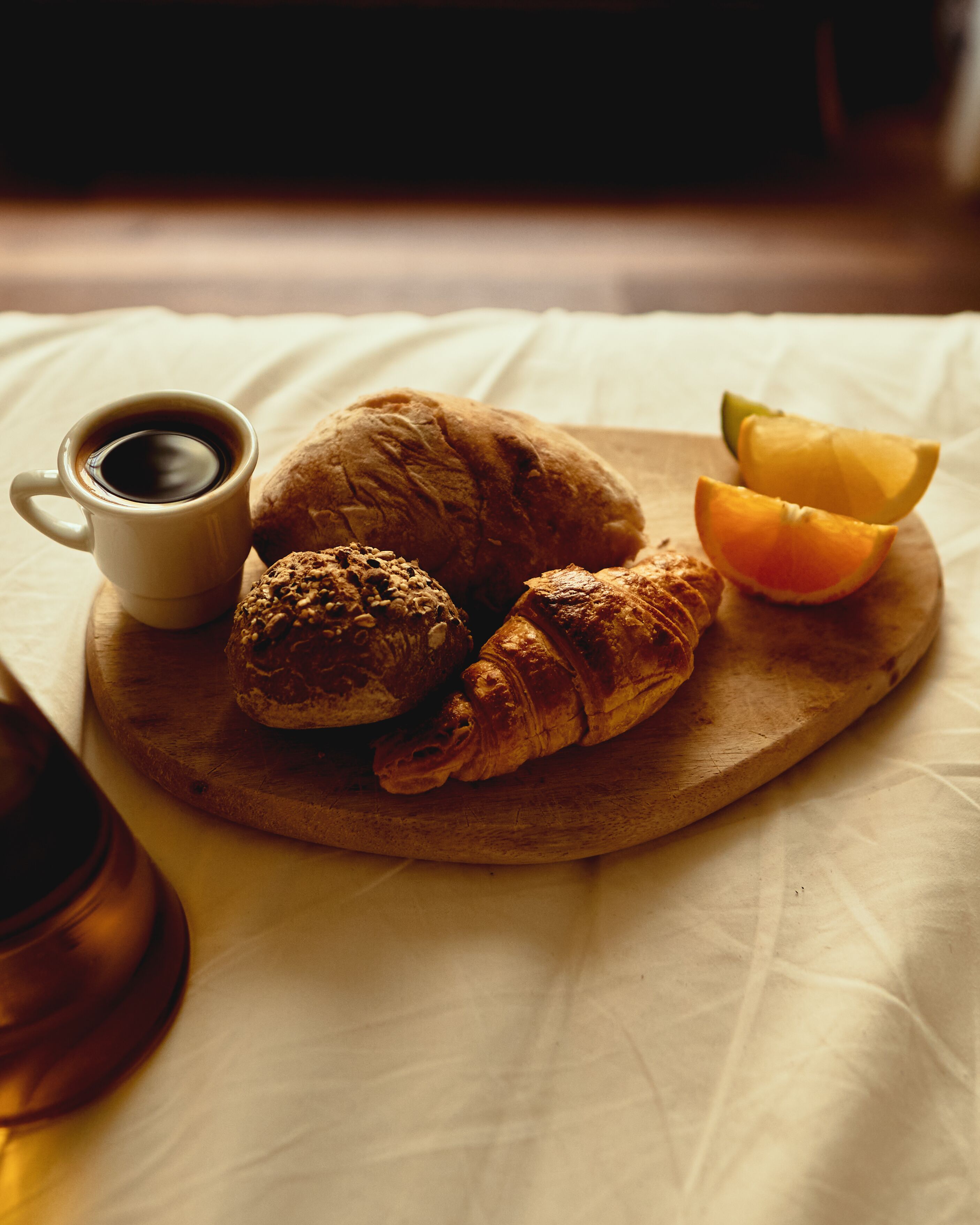 A wooden board with a croissant, a muffin, and a half orange on a white tablecloth.