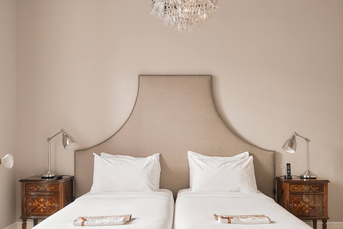 Un lit double avec une tête de lit beige, deux tables de chevet avec des lampes et un lustre.