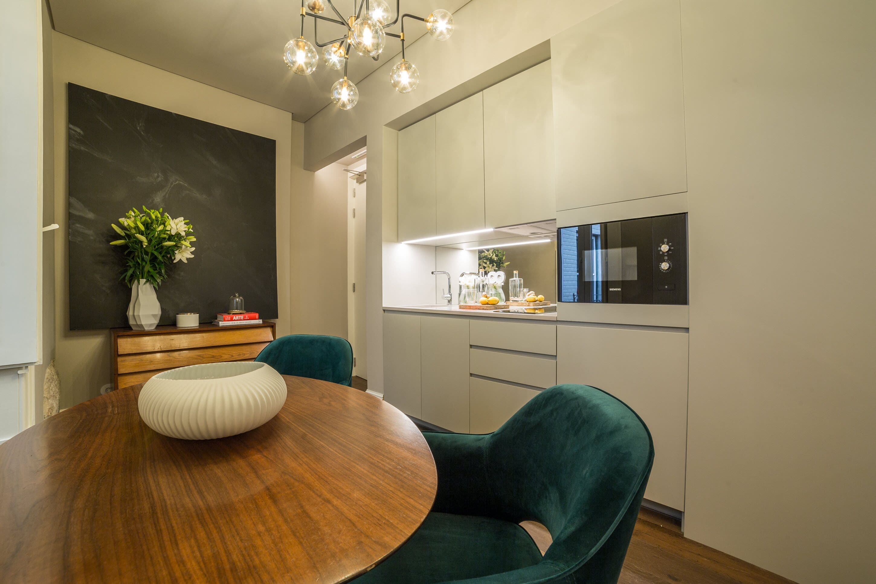 A modern dining area with a wooden table, teal chairs, and a black vase with flowers.