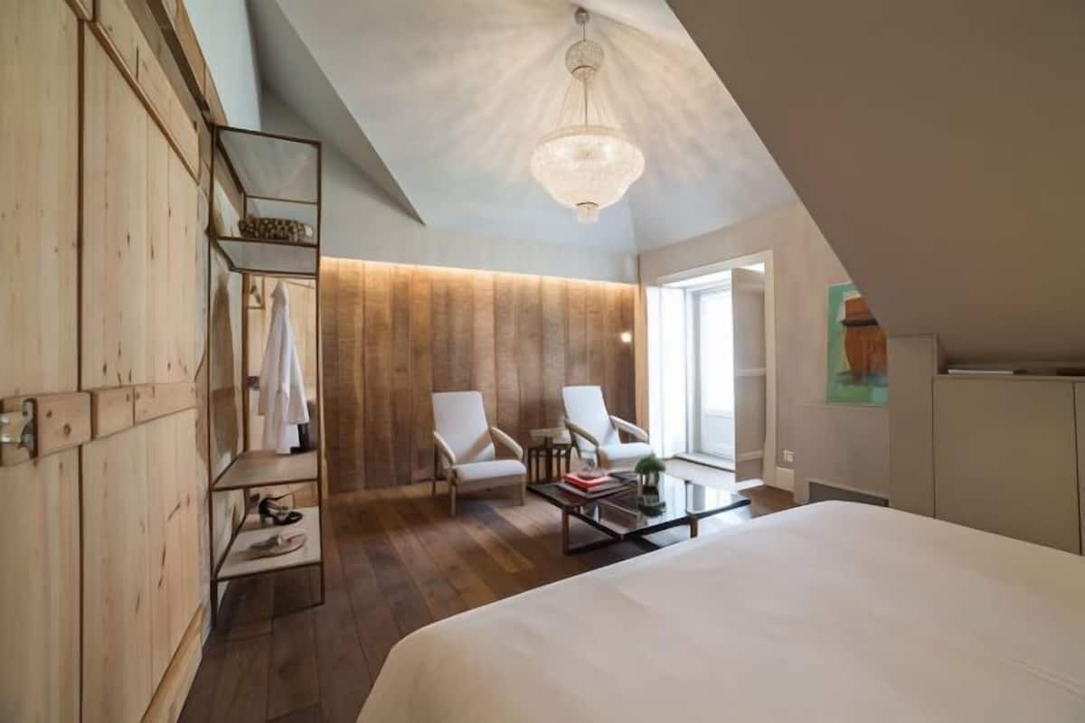 Une chambre à coucher avec un grand lit, deux chaises, une petite table et une armoire en bois.