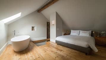 A bedroom with a large bed, a built-in bathtub, and a sloped ceiling.