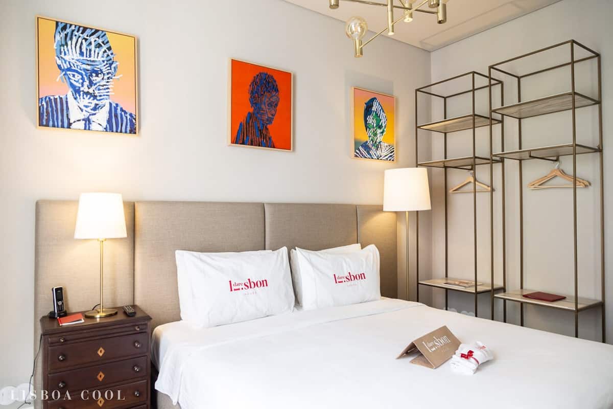 Une chambre d’hôtel avec un lit, deux lampes de chevet, une table de chevet avec un téléphone et un livre, et des œuvres d’art murales.