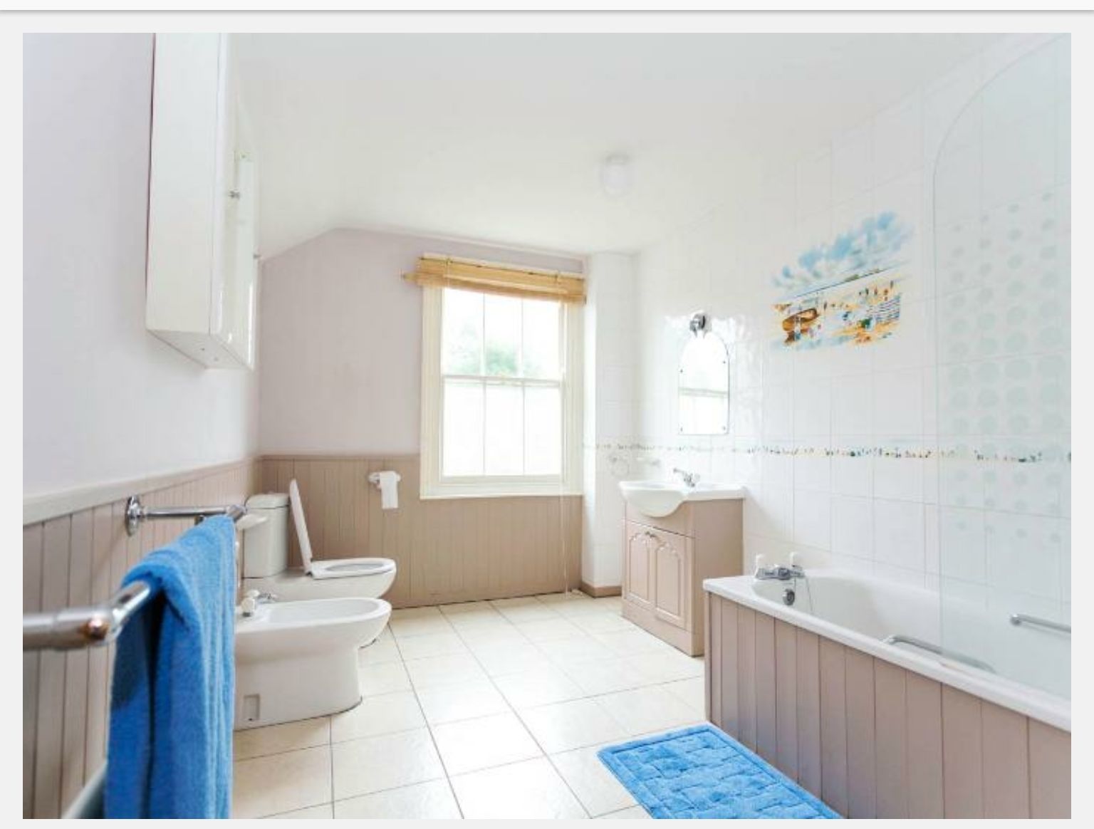 Un bany amb dues vàteres, un lavabo, una banyera i una finestra amb cortina.