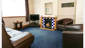 A living room with a fireplace, a television, and two leather sofas. - Fishermen's Cottage (Deal)