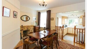A dining room with a wooden table and chairs, a fireplace, and a chandelier. - Fishermen's Cottage (Deal)