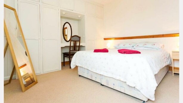 A bedroom with a bed, a chair, a mirror, and a bedside table. - Fishermen's Cottage (Deal)