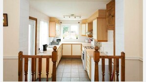 A kitchen with wooden cabinets, a central island, and a view to the outside. - Fishermen's Cottage (Deal)