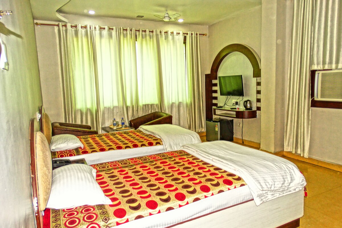 A hotel room with two beds, a desk with a television, and a small kitchenette.