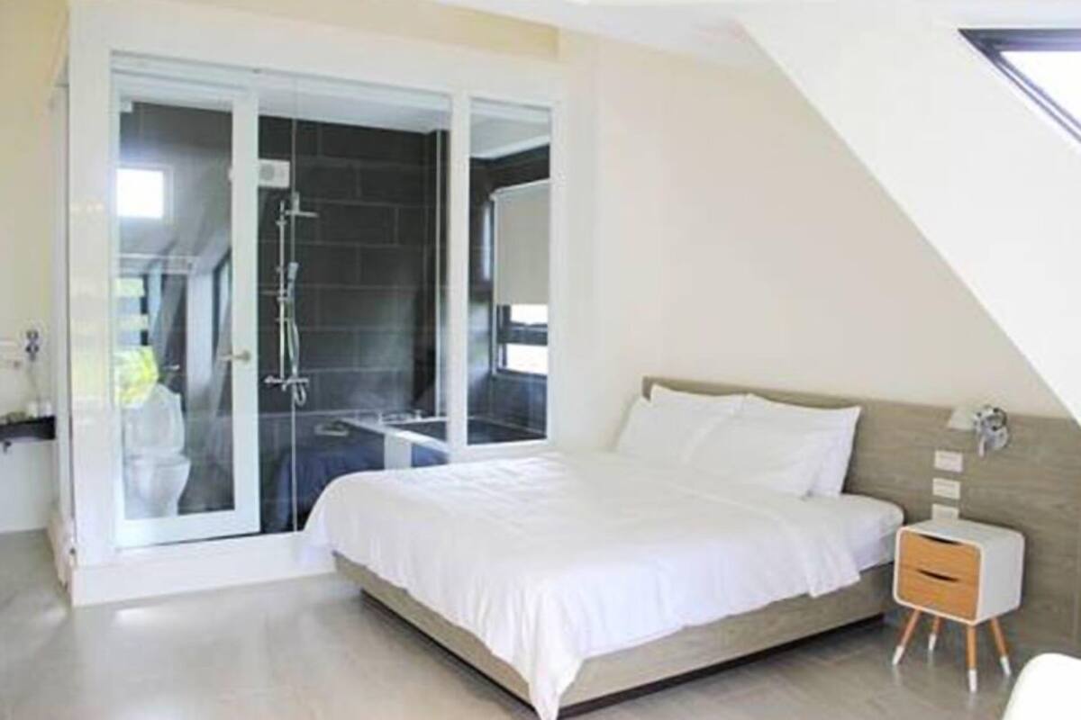 A modern bedroom with a large bed, a bedside table, and a glass shower enclosure.